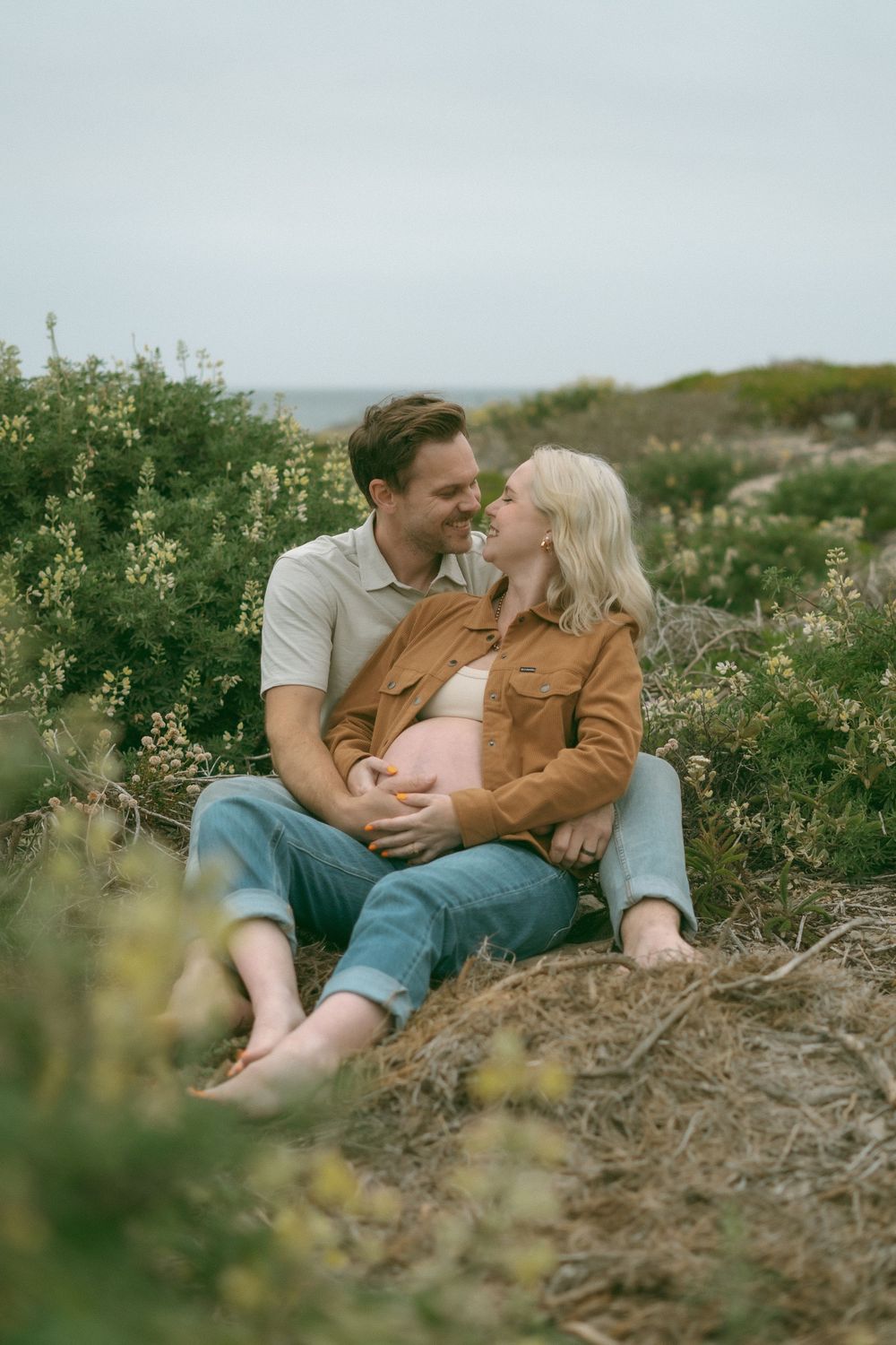 Happy couple sitting outdoors, woman cradling pregnant belly.