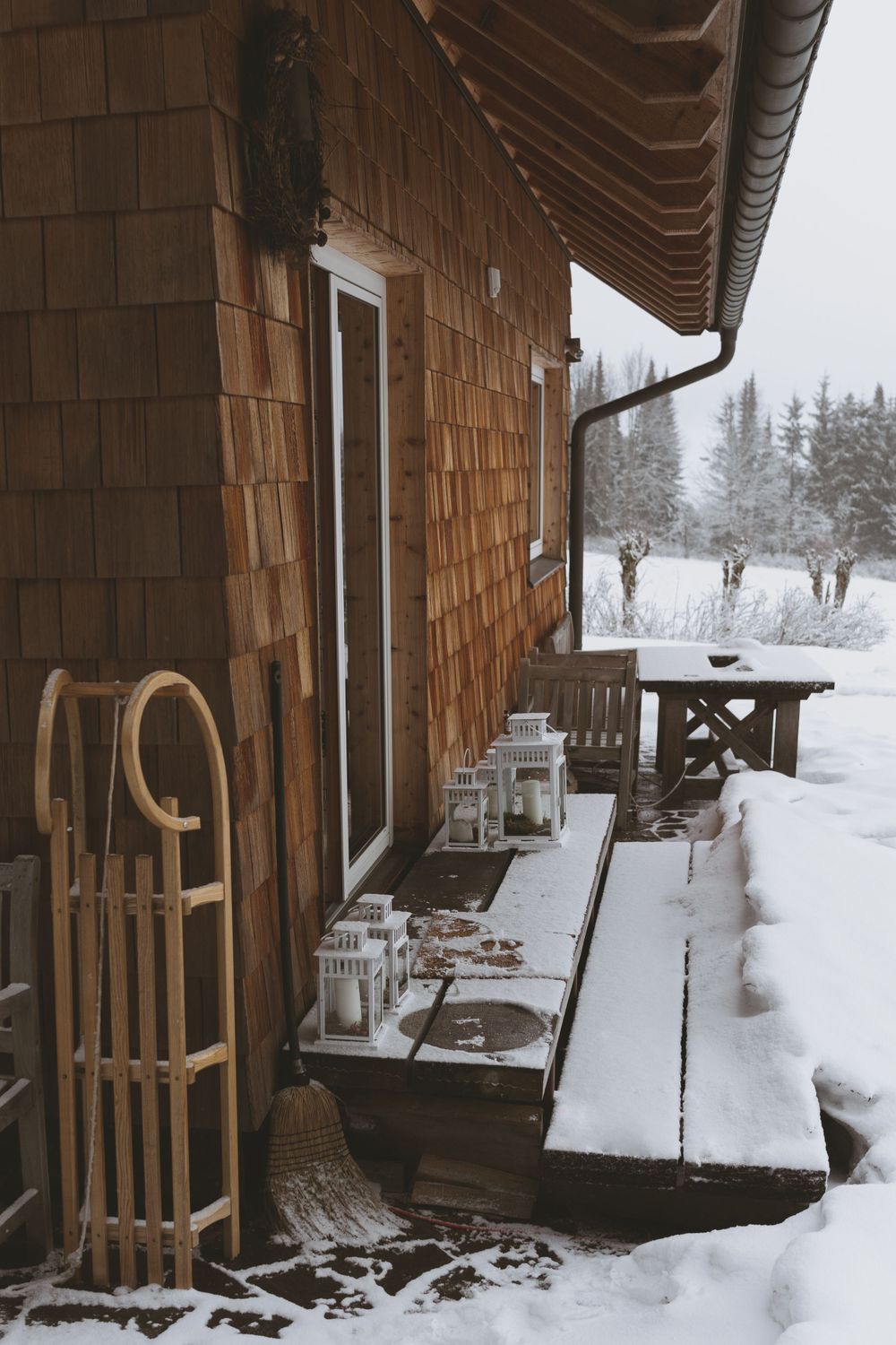 Vintage wooden sled and lanterns on snow-covered porch of rustic cabin.