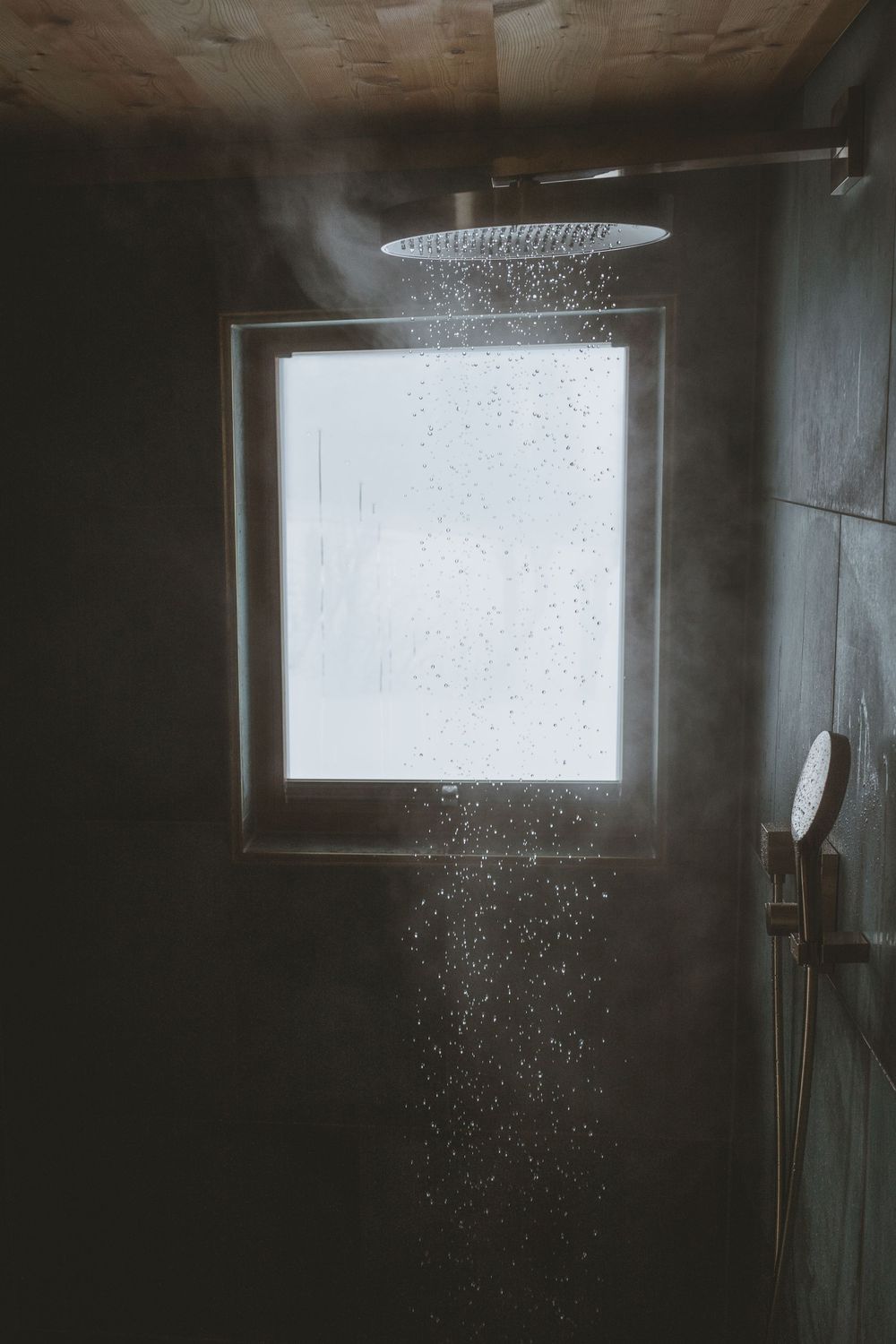Steam rising from a modern rainfall shower head in a bathroom with a frosted window.