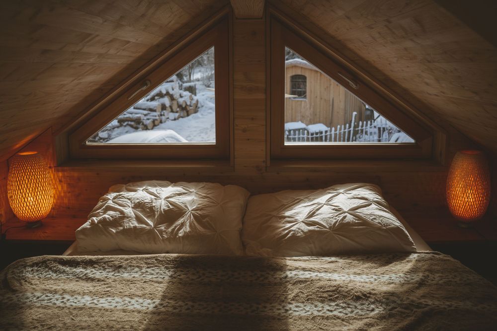 Cozy bedroom with triangular windows and ambient lighting showing snowy scene outside.
