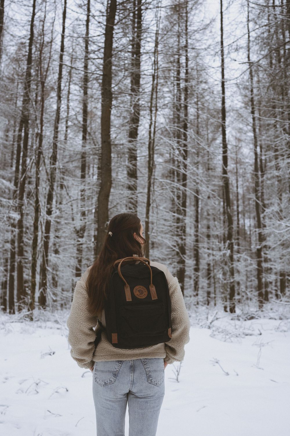 Person with backpack walking through snow-covered forest trail in winter.