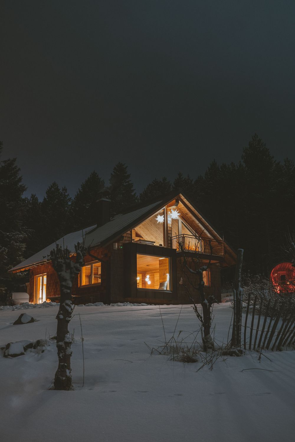 Illuminated wooden cabin glowing warmly in snowy winter night landscape.