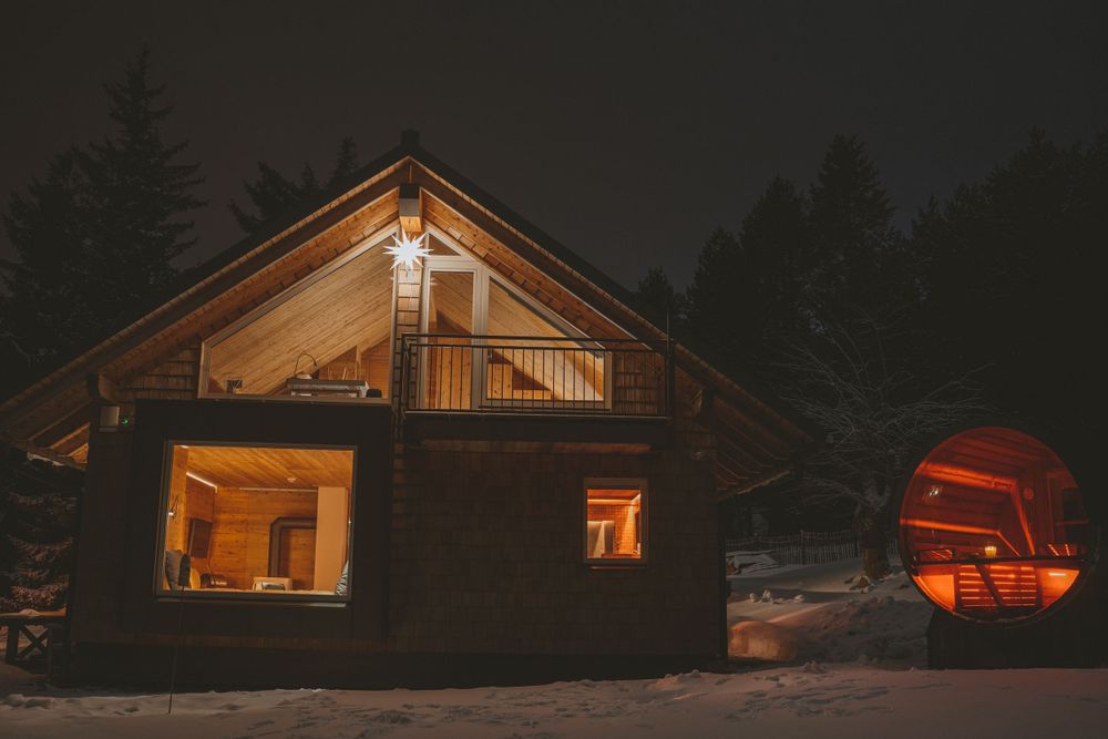 Cozy wooden cabin illuminated at night with warm interior lighting and a glowing red sphere structure nearby.