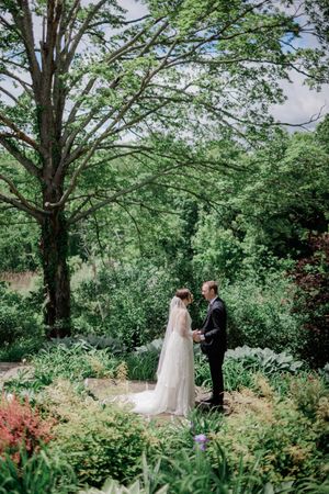 A bride and groom share a romantic moment in a lush garden, surrounded by vibrant greenery and colorful flowers.