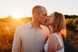 Couple sharing a romantic kiss at golden sunset in an outdoor field, warm sunlight glowing behind them.