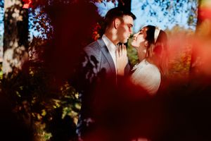 Couple sharing a romantic moment outdoors, framed by vibrant red autumn foliage and sunlit trees.