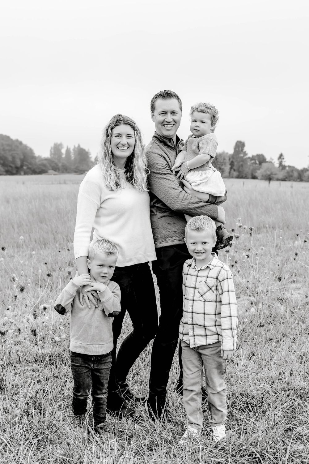 Black and white portrait of a smiling family of five standing together in an open field.