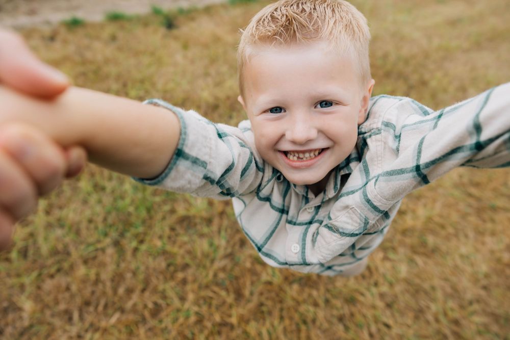 Joyful young boy smiling while being swung around outdoors in a grassy field.