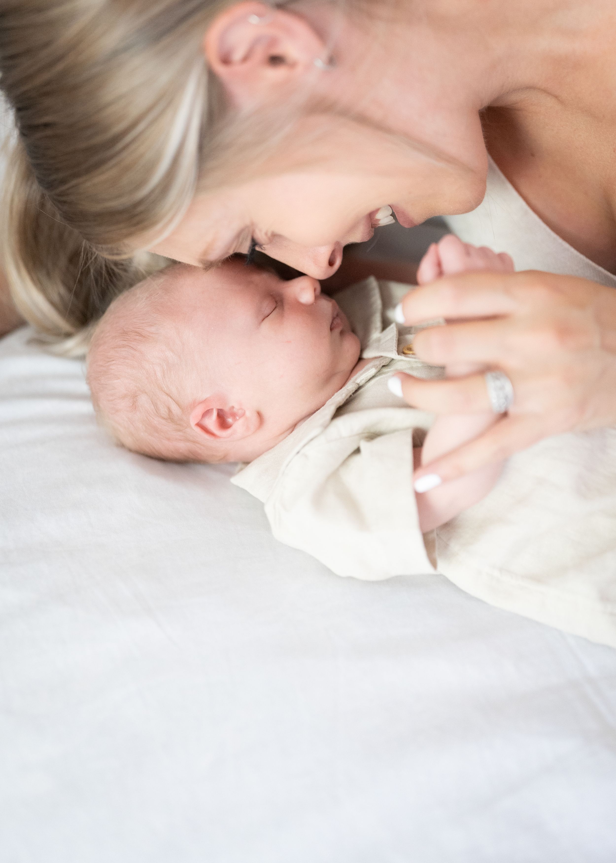 Intimate moment between mother and newborn baby in soft natural light against white bedding.