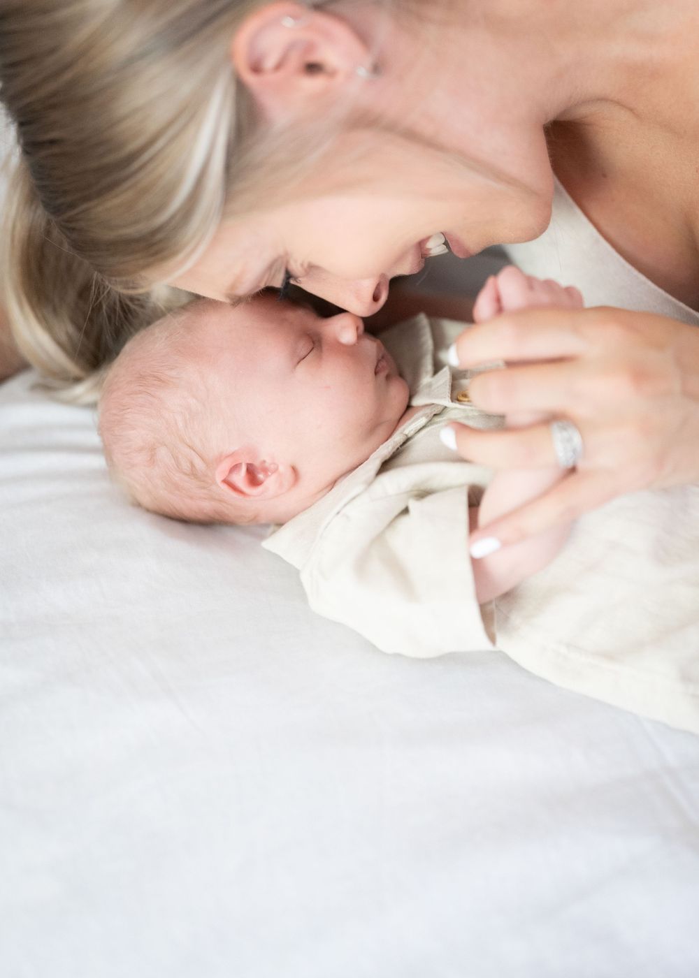 Intimate moment between mother and newborn baby in soft natural light against white bedding.