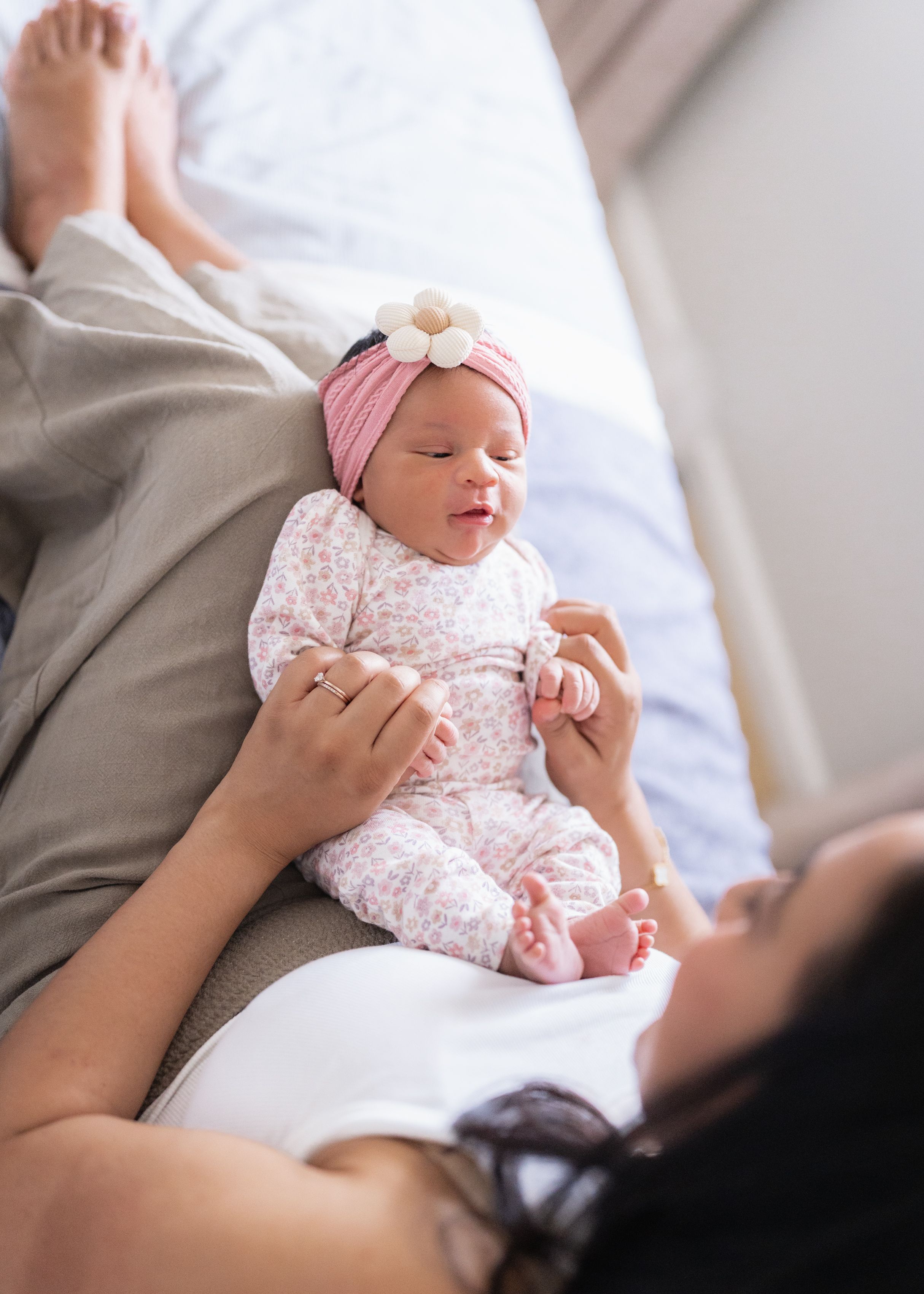 A baby wearing a pink headband and floral dress rests peacefully on a white surface.