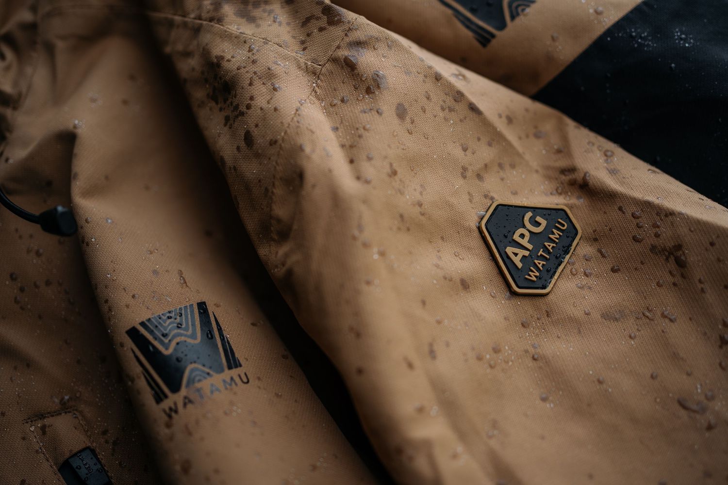 Close-up of tan ARG Wairau branded jacket with hexagon logo patch, featuring dirt splatter details.