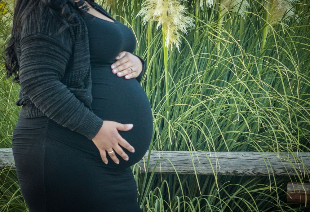 Close up of pregnant belly against natural grass backdrop.