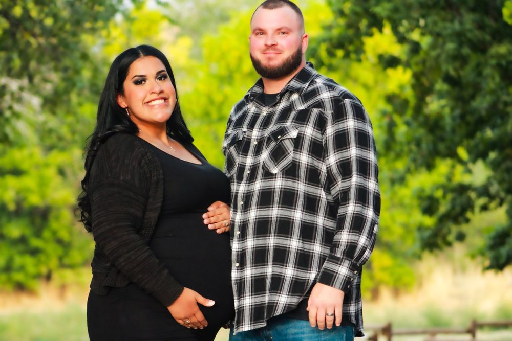 Outdoor maternity portrait of couple against green foliage.