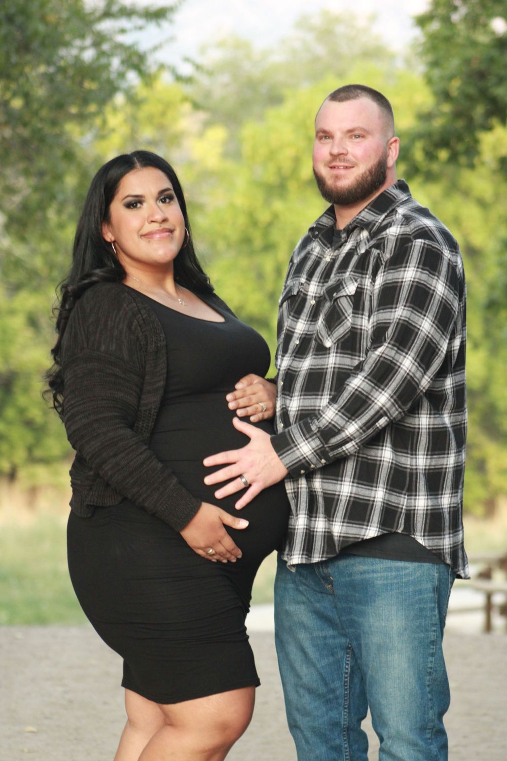 A pregnancy photoshoot featuring a couple in a park setting with the woman wearing a black dress.