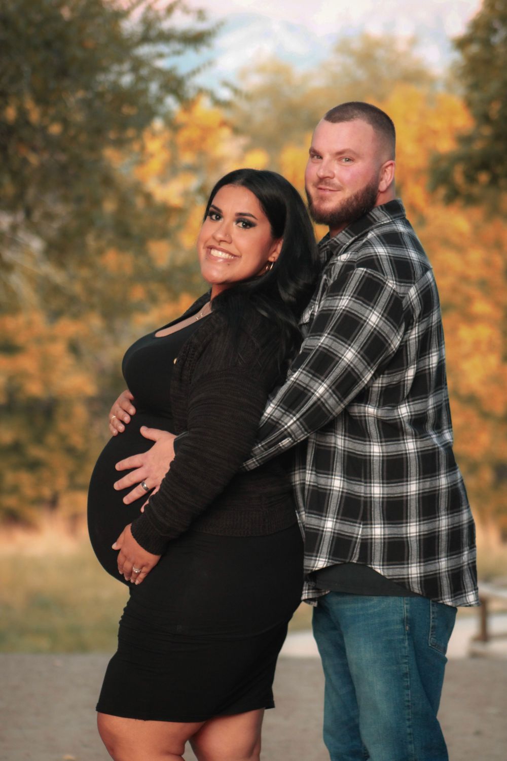 An autumn maternity photo session with a couple posing outdoors among fall foliage.