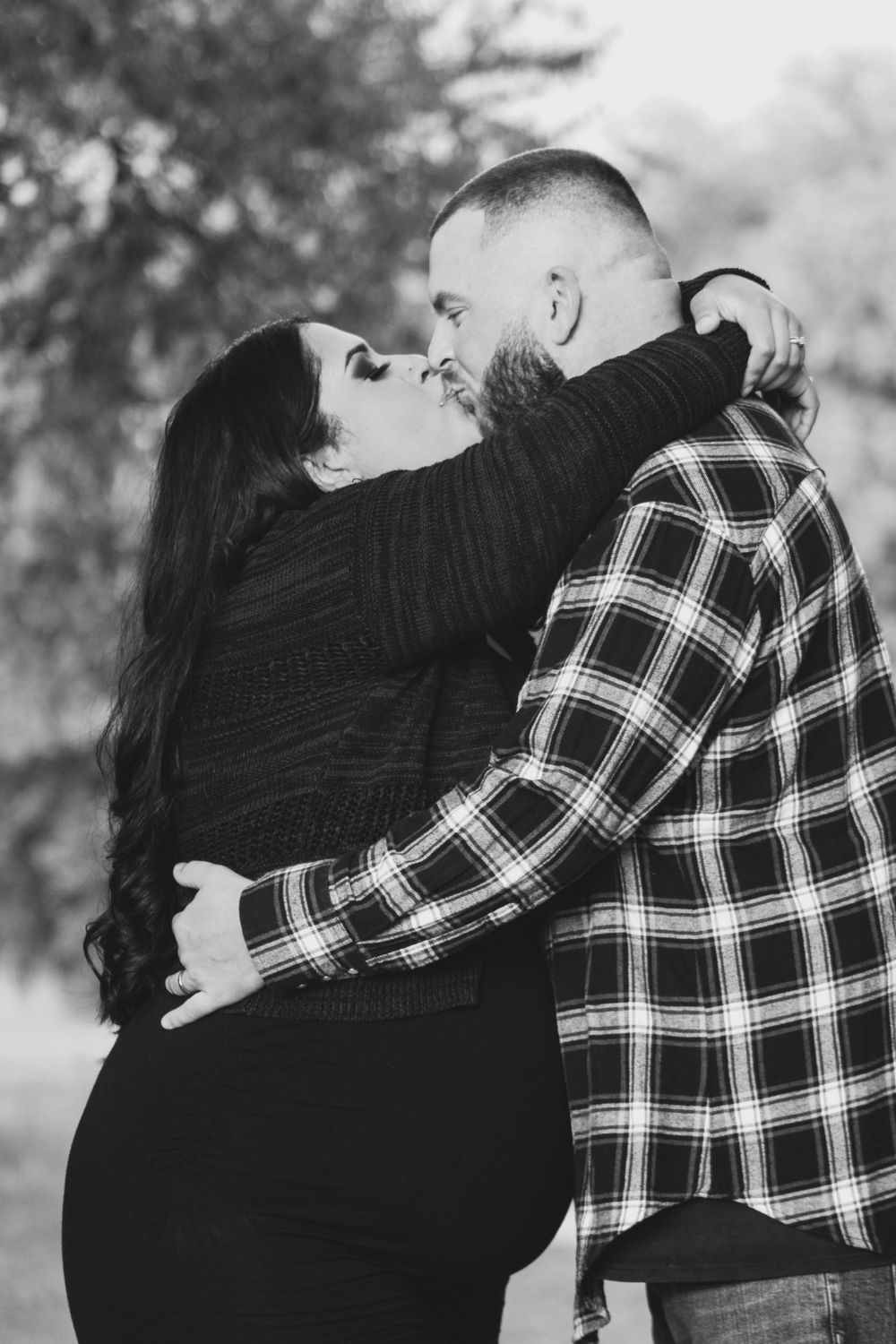 An intimate black and white maternity photo of a couple embracing outdoors.