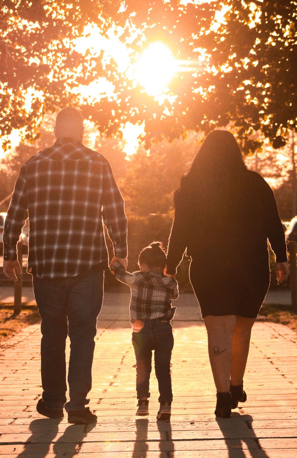Family silhouette walking together at sunset with toddler between parents.