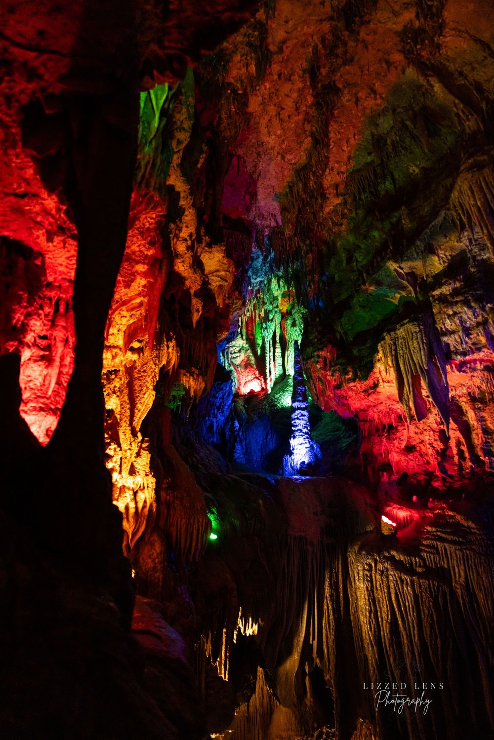 Colorful illuminated stalactites and stalagmites reflected in a cave pool.