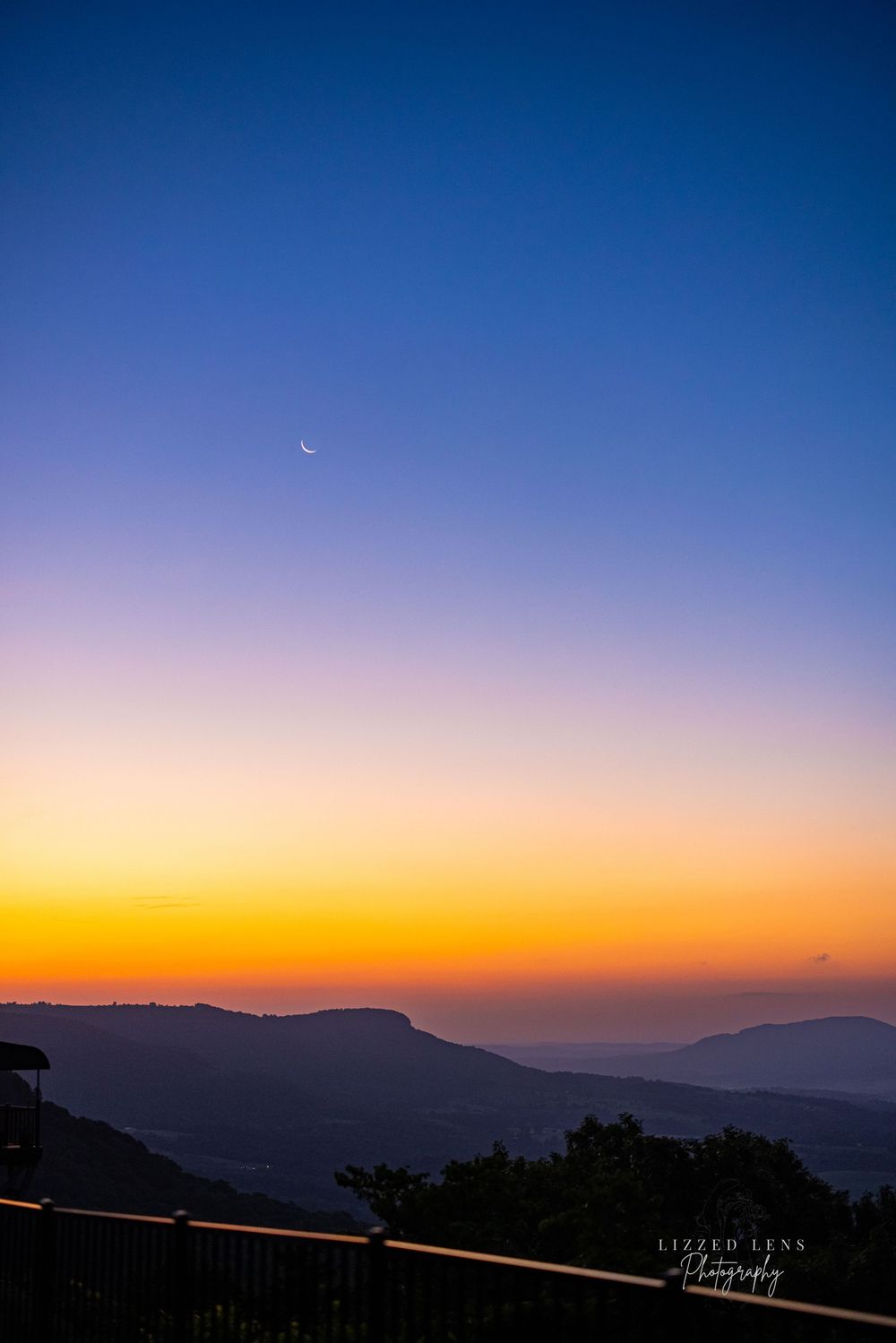 Crescent moon over colorful mountain sunset with orange and blue gradient sky at dusk.