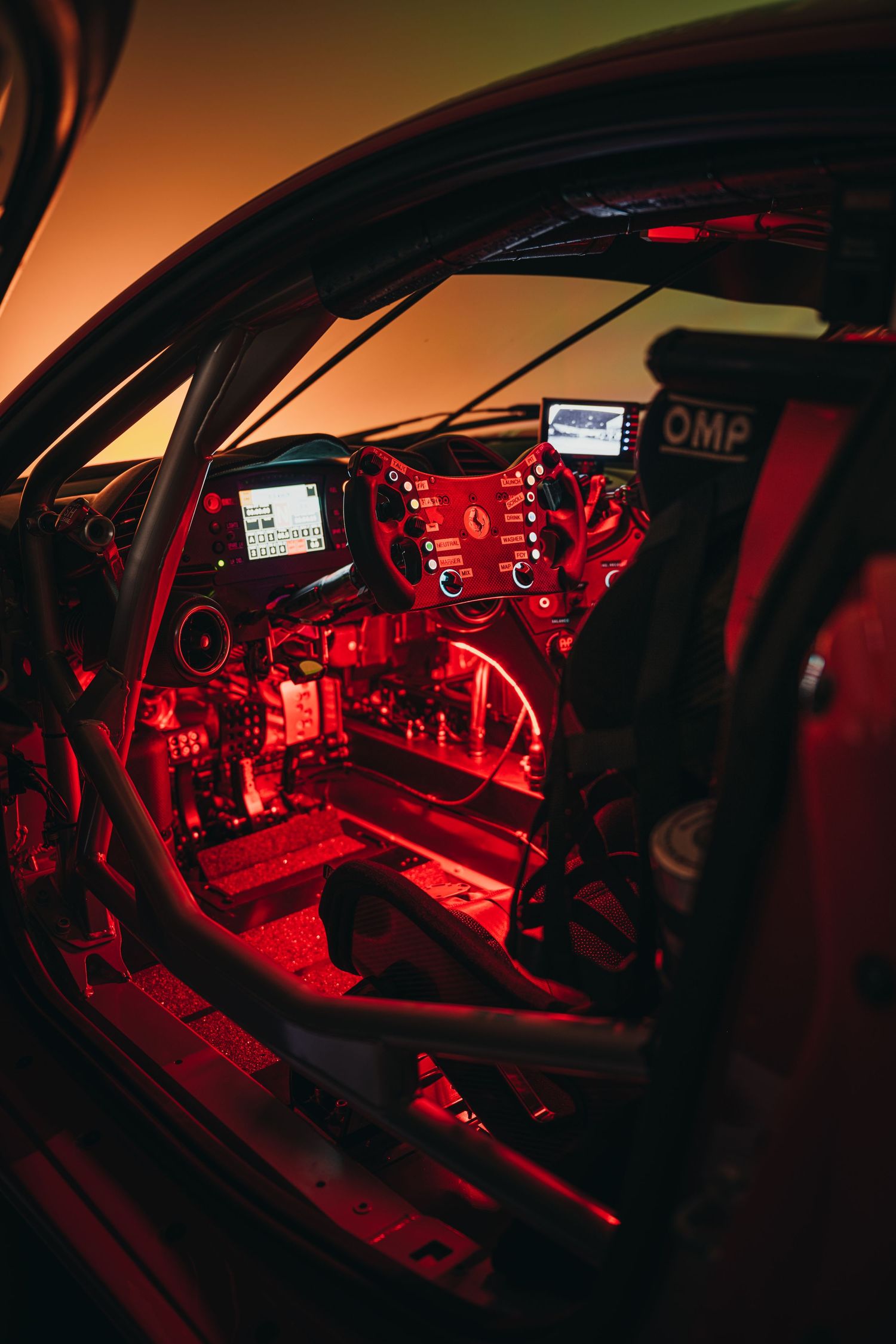 Race car interior illuminated with dramatic red lighting showing detailed cockpit controls.