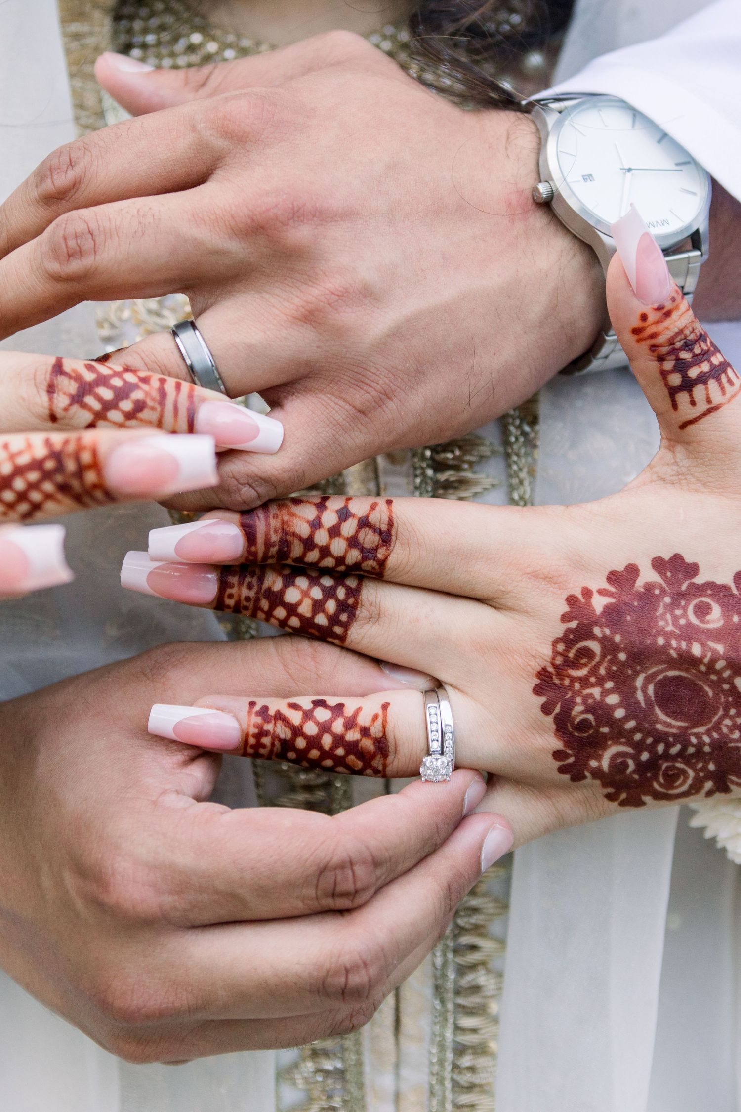 Close-up of hands exchanging rings with intricate henna designs during a wedding ceremony.