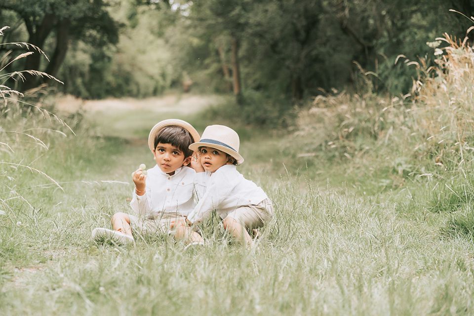 two cute little boys in hats in the park interacting and bonding amongst a field of long wheat strands