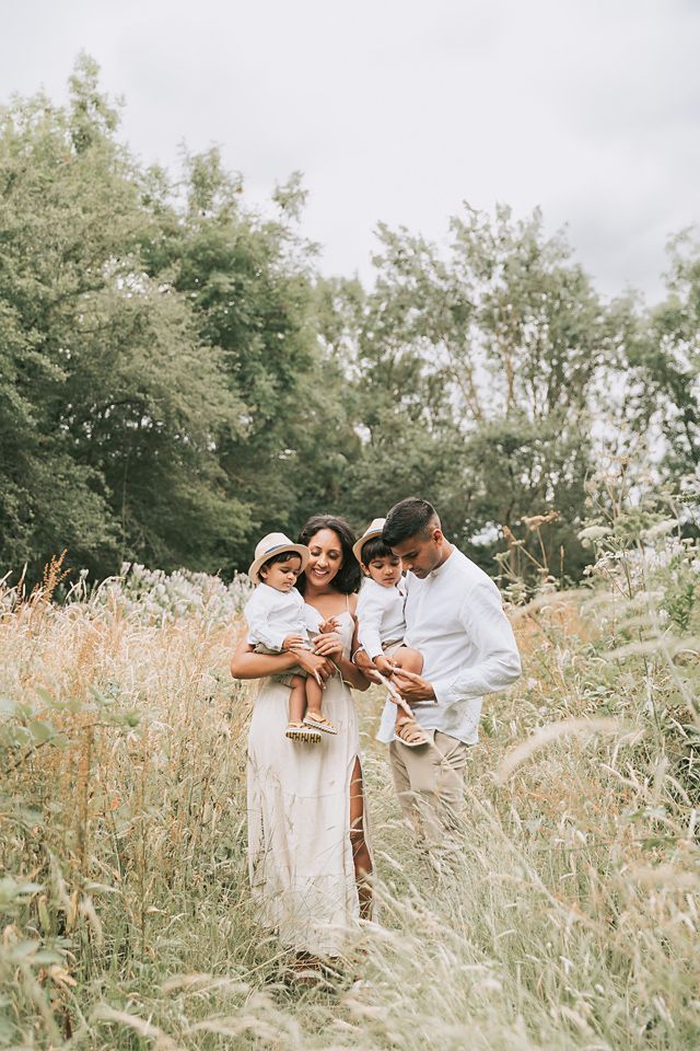 Family of four in the park interacting and bonding amongst a field long wheat strands two little boys in hats