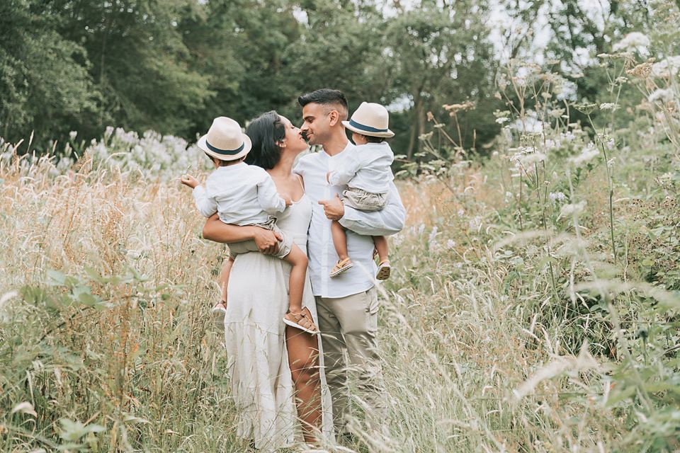 Family of four in the park with mom and dad interacting and bonding amongst a field long wheat strands