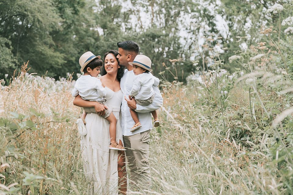 Family of four in the park interacting and bonding amongst a field long wheat strands two little boys in hats