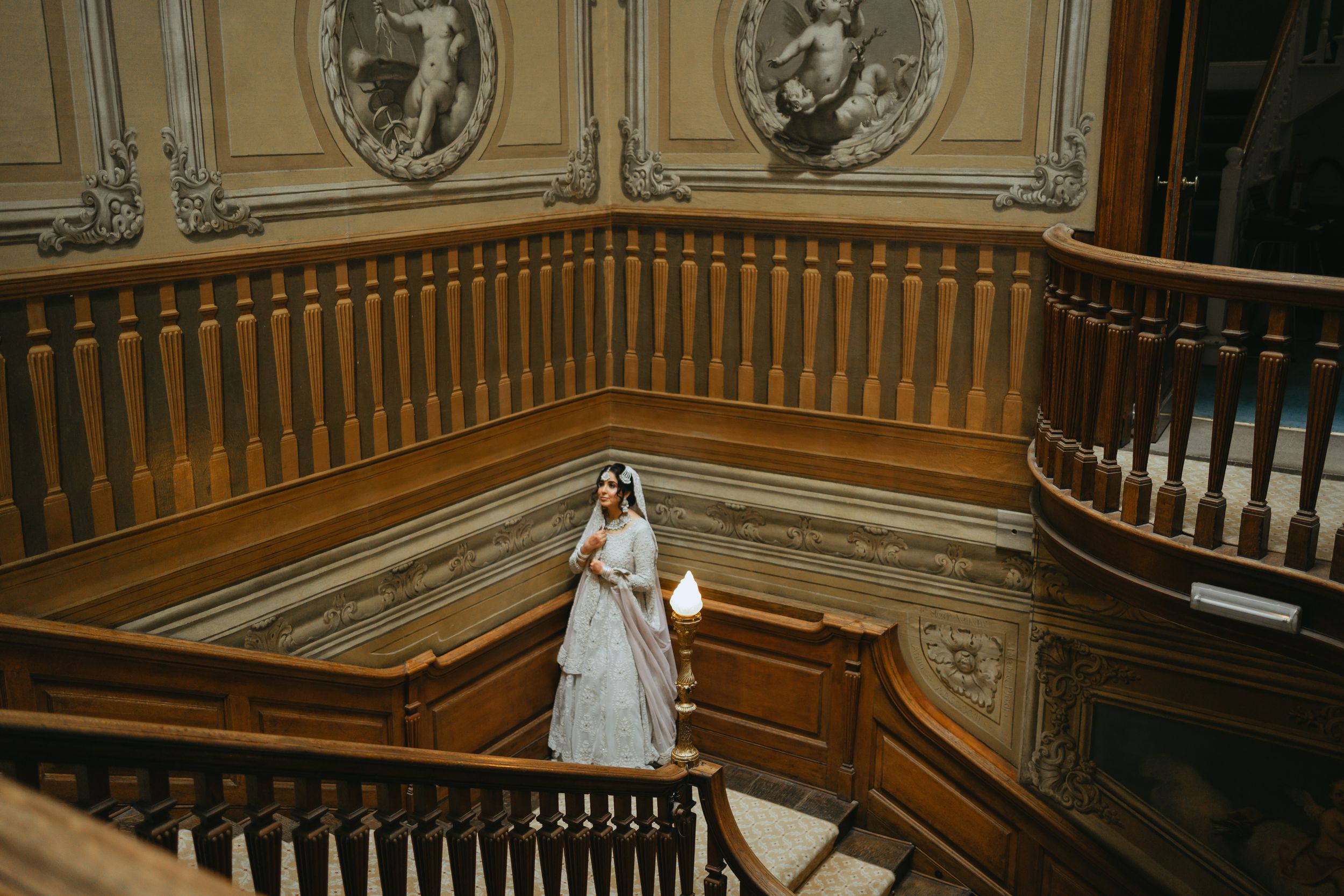 Ornate wooden staircase with decorative carved railings and medallion details in a historic mansion interior.