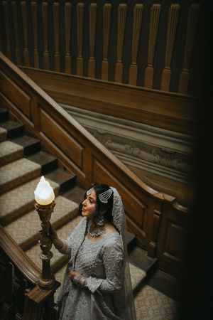 Dramatic lighting illuminates a person in a gray dress and veil sitting in ornate wooden church pews.