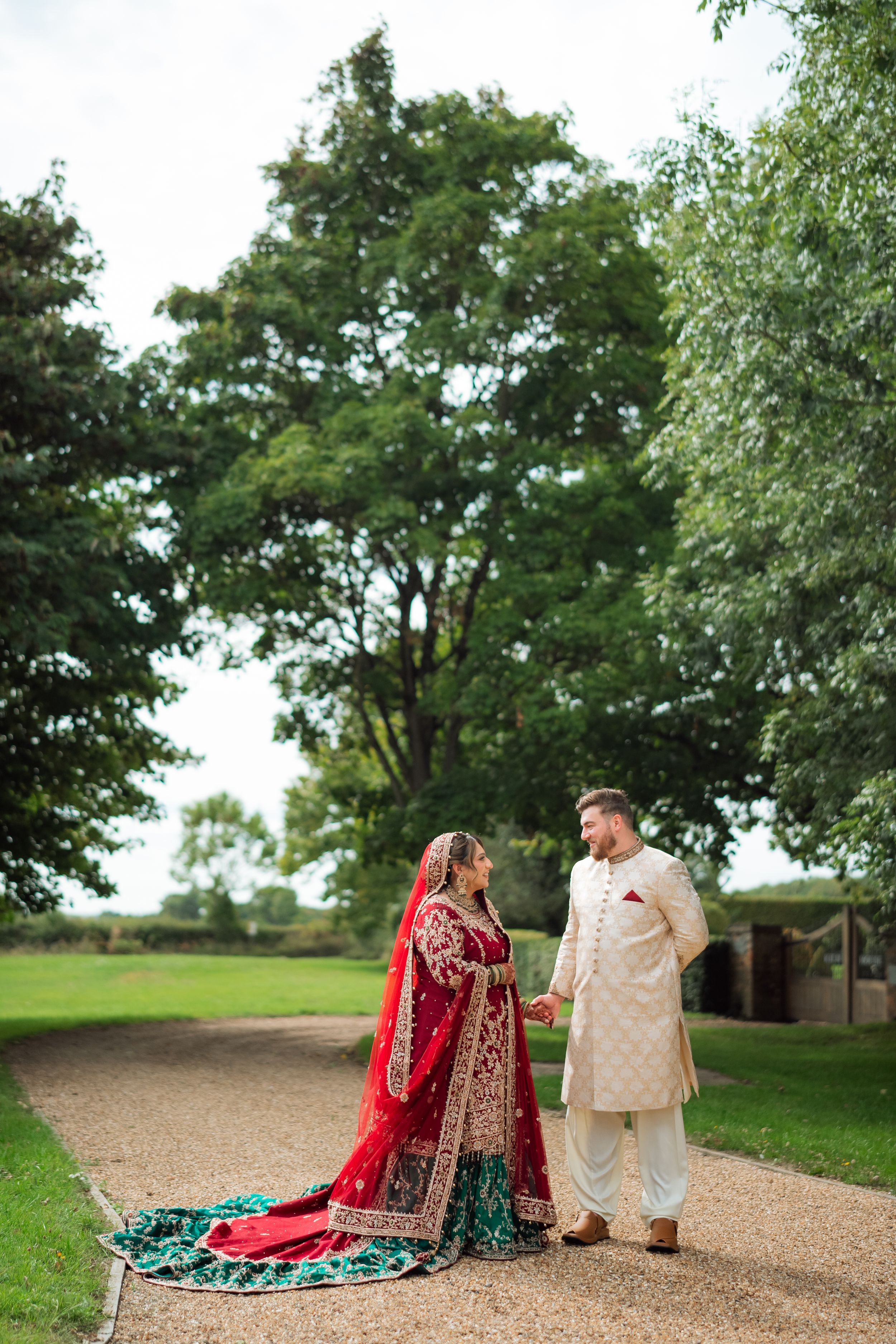 A couple in traditional South Asian wedding attire share a romantic moment on a grassy hill overlooking a scenic landscape.