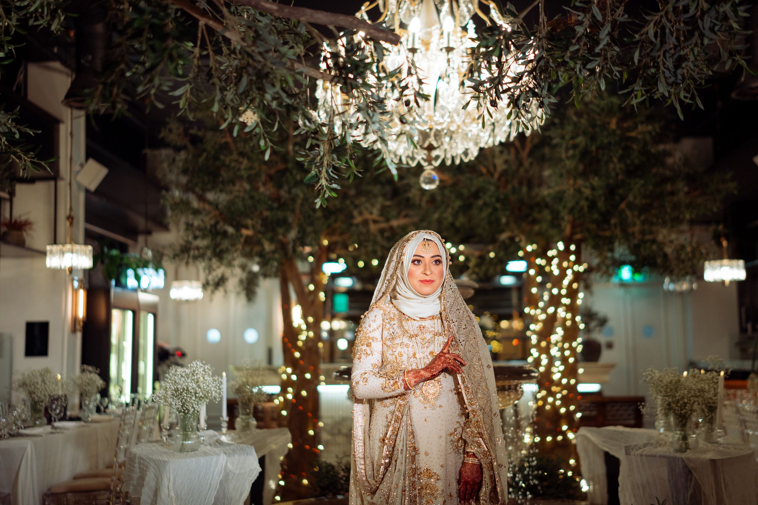 An elegant indoor wedding reception venue decorated with crystal chandeliers, trees, and twinkling lights.