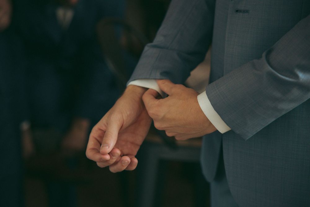 Close-up of folded hands in grey suit sleeves during wedding ceremony.