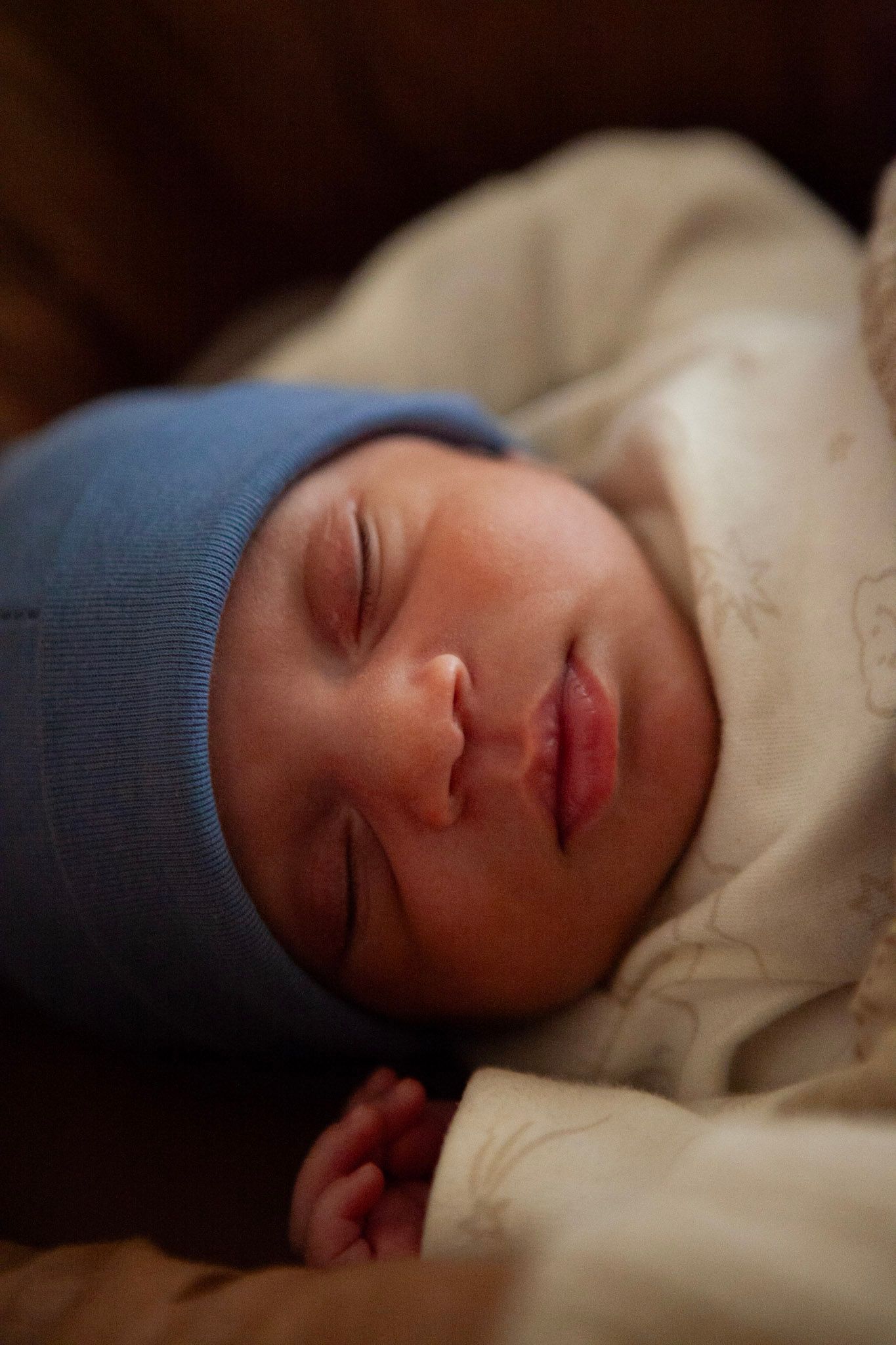 A sleeping baby wearing a blue cap rests peacefully on white bedding.