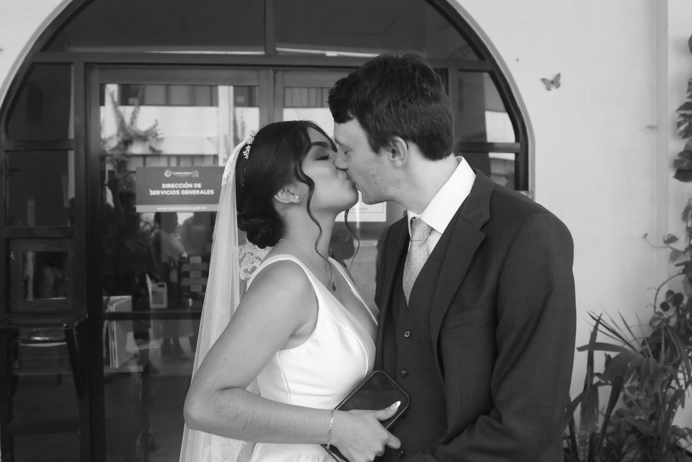 Black and white photo of a bride and groom sharing their first kiss at a wedding ceremony outdoors.