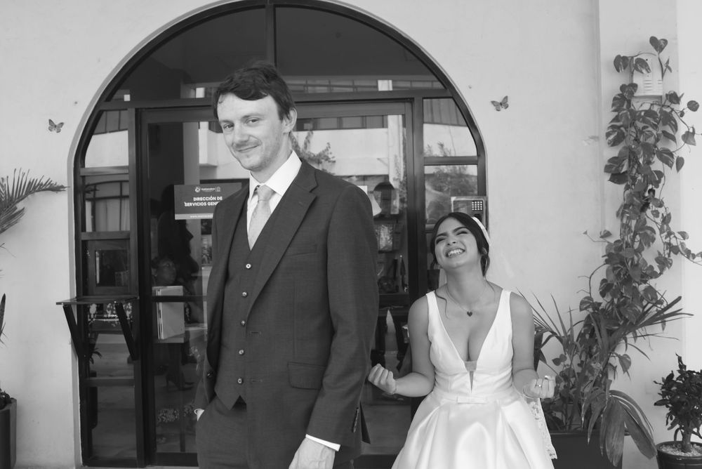 Black and white wedding photo of a tall groom in a suit and bride in a white dress walking together outside a building.