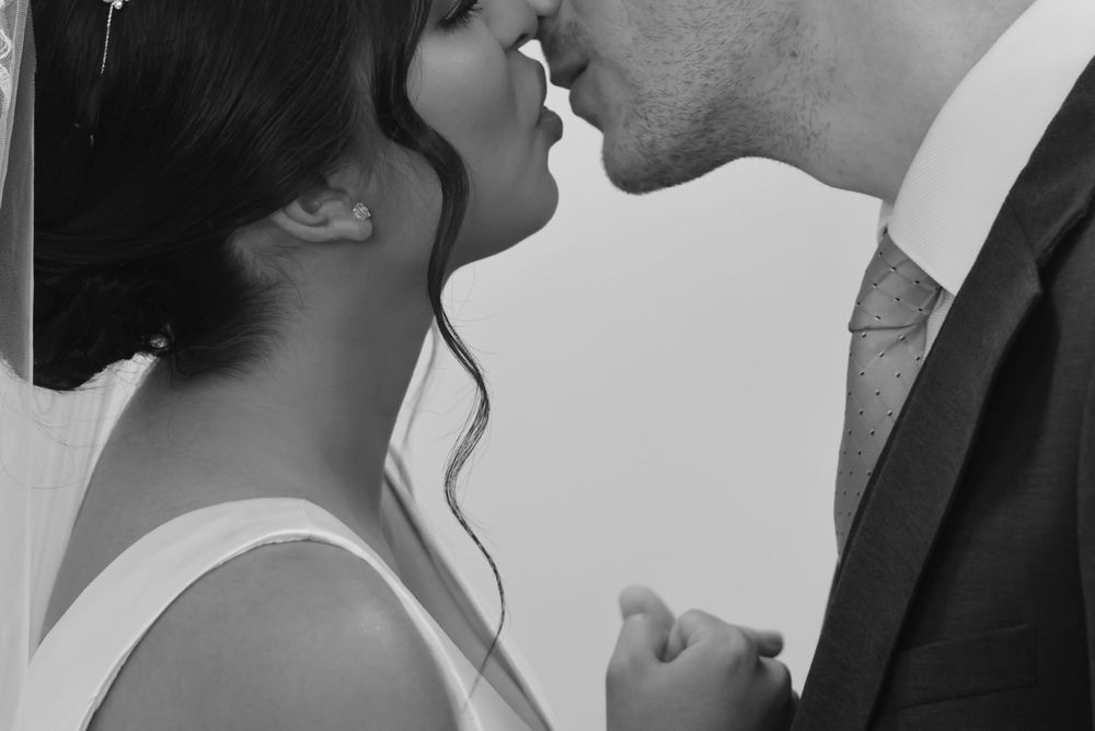 Black and white photo of a bride and groom sharing a romantic kiss on their wedding day.