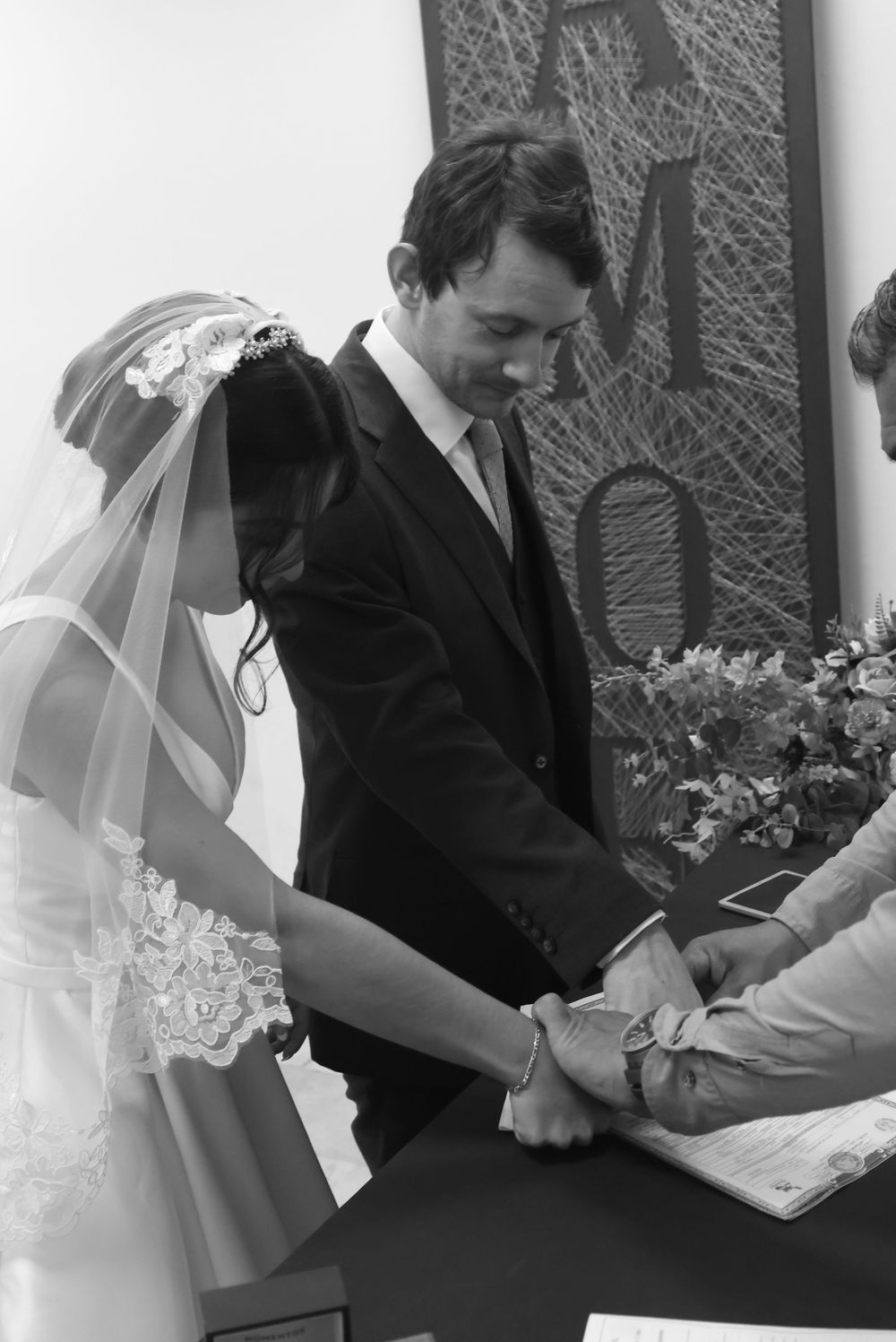 Black and white photo of a bride and groom signing their marriage certificate at their wedding ceremony.