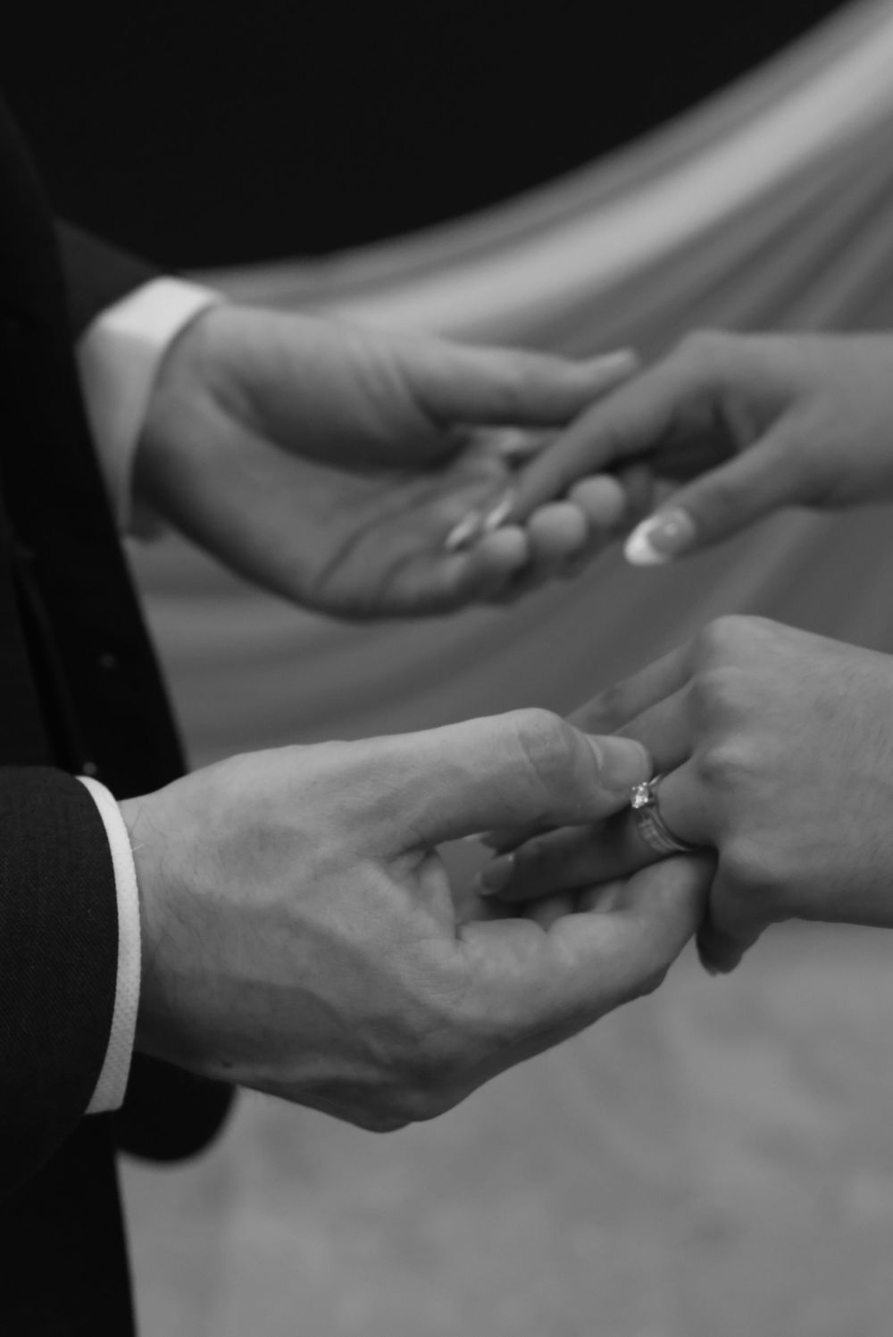 Black and white photo of groom placing wedding ring on bride's finger during ceremony.