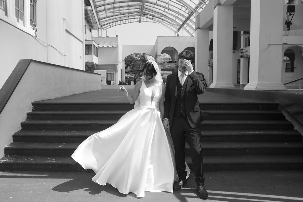 Black and white photo of a bride in a flowing white gown and groom in a suit walking together on outdoor steps.