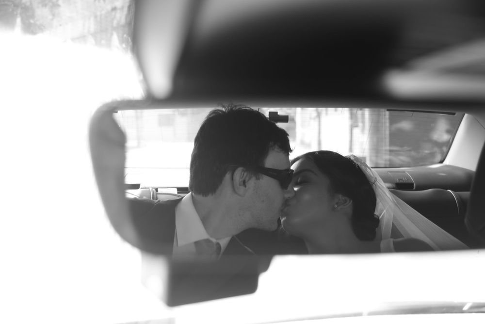 Black and white photo of a couple kissing in a car, captured through the rearview mirror on their wedding day.