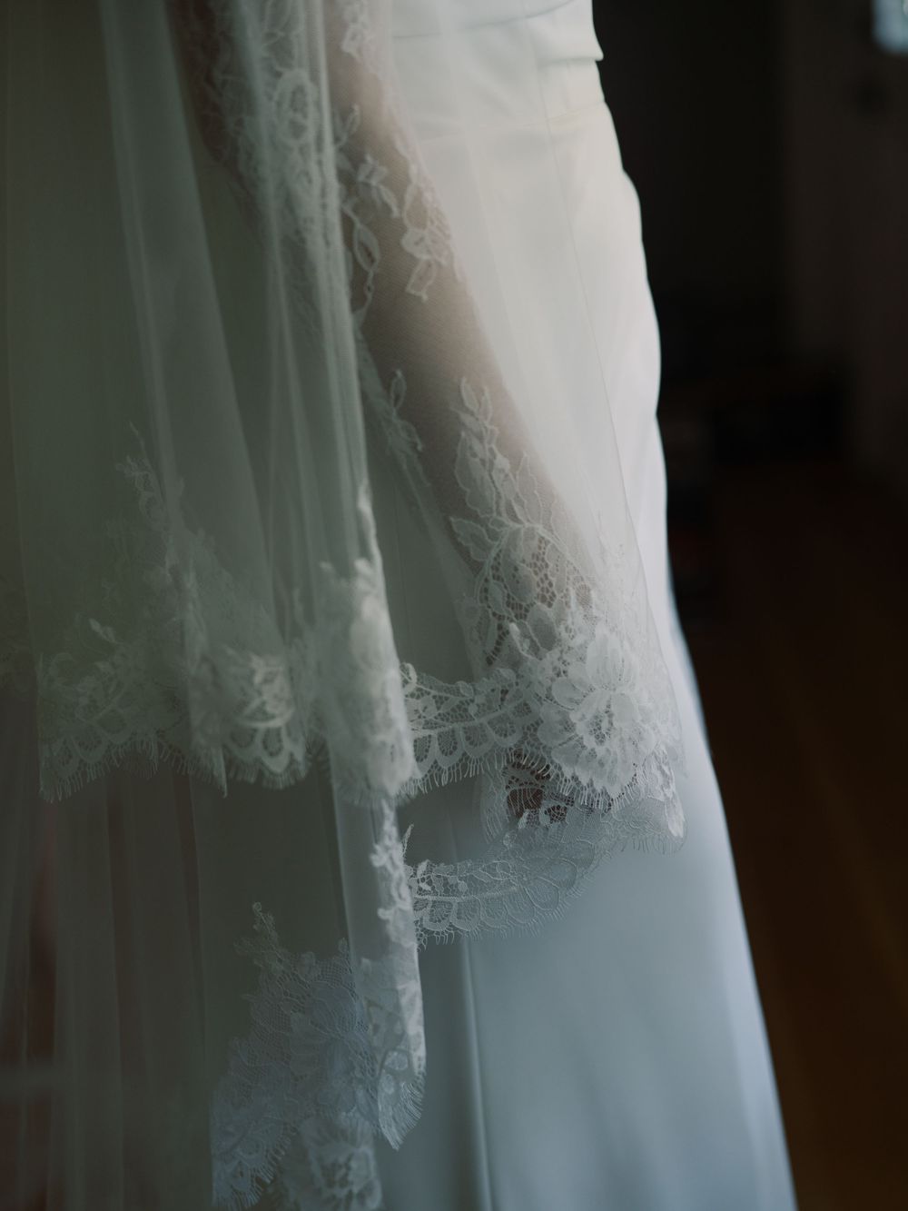 Close-up of a white wedding dress with delicate lace trim and flowing tulle veil hanging elegantly indoors.