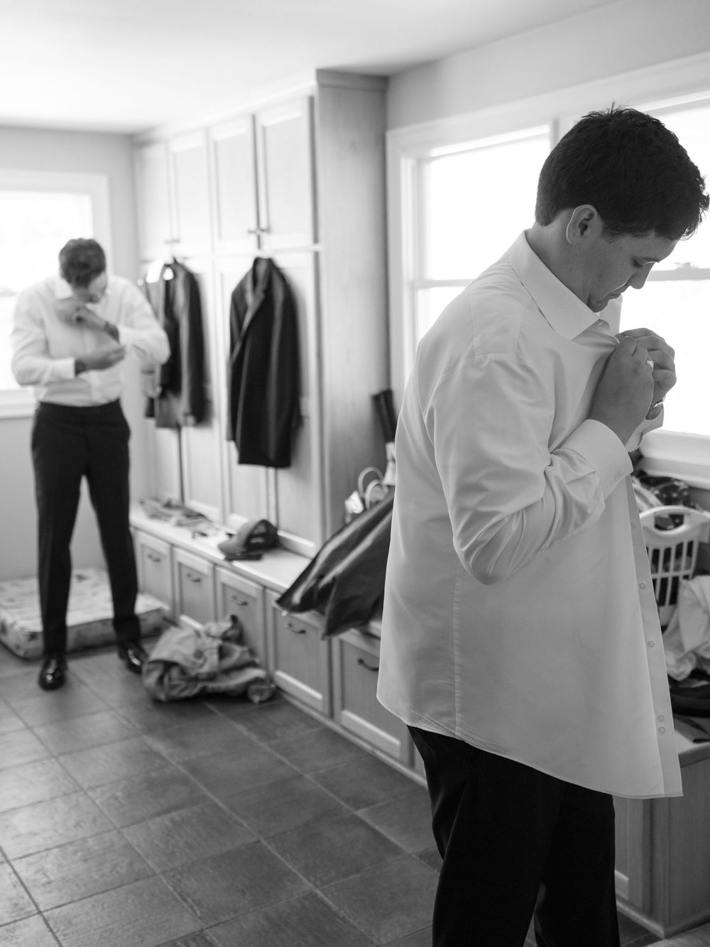 Two groomsmen in white dress shirts preparing for a wedding ceremony in a black and white photo.