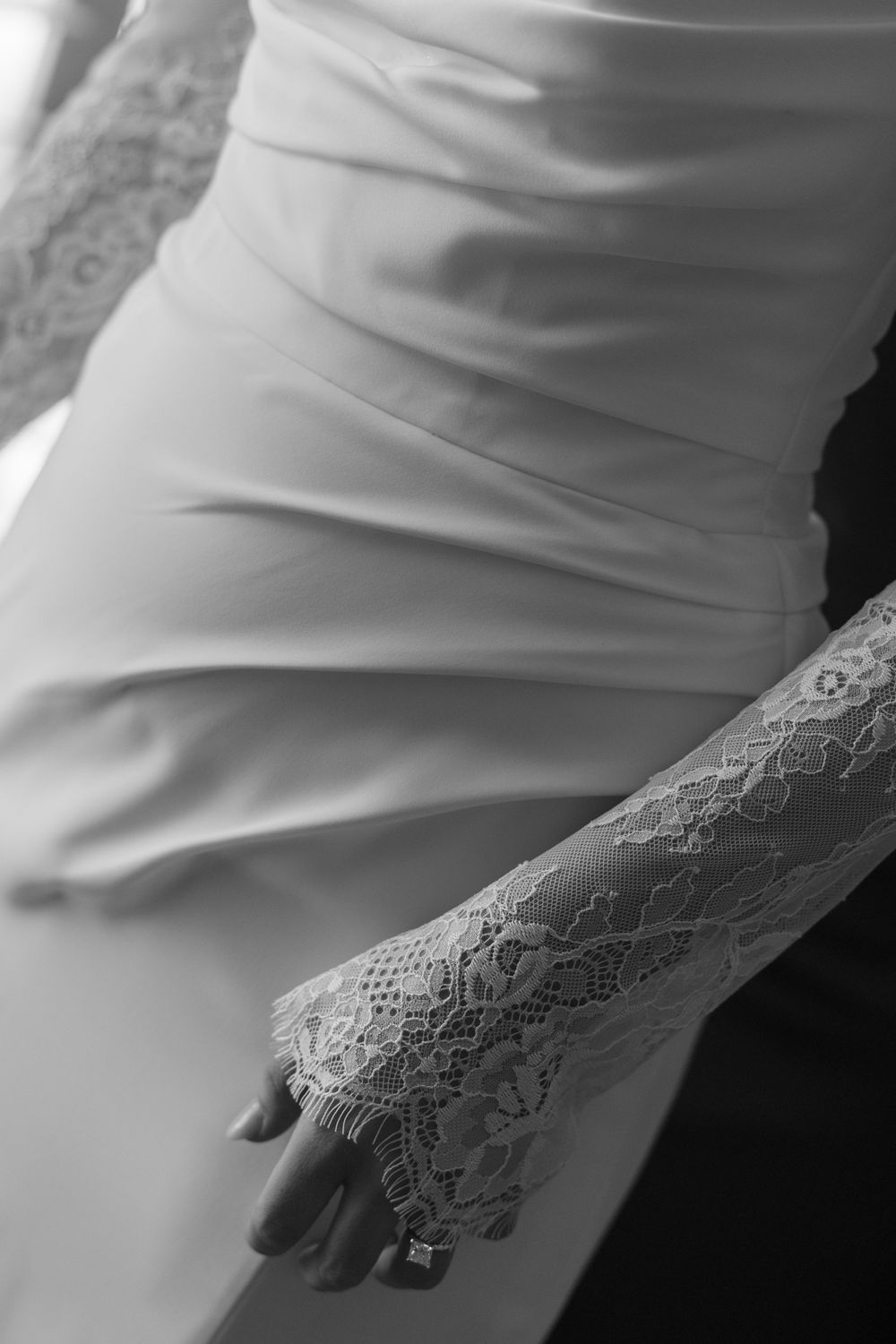 Close-up black and white photo of a bride in a satin wedding gown with elegant lace sleeves and a diamond ring.