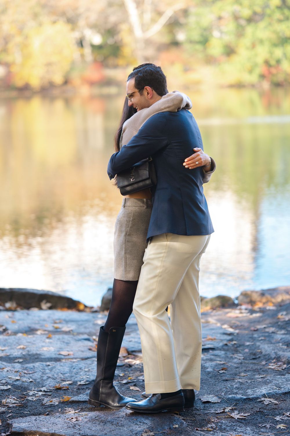 Couple embracing in a warm hug by a reflective autumn lake, surrounded by colorful fall foliage.