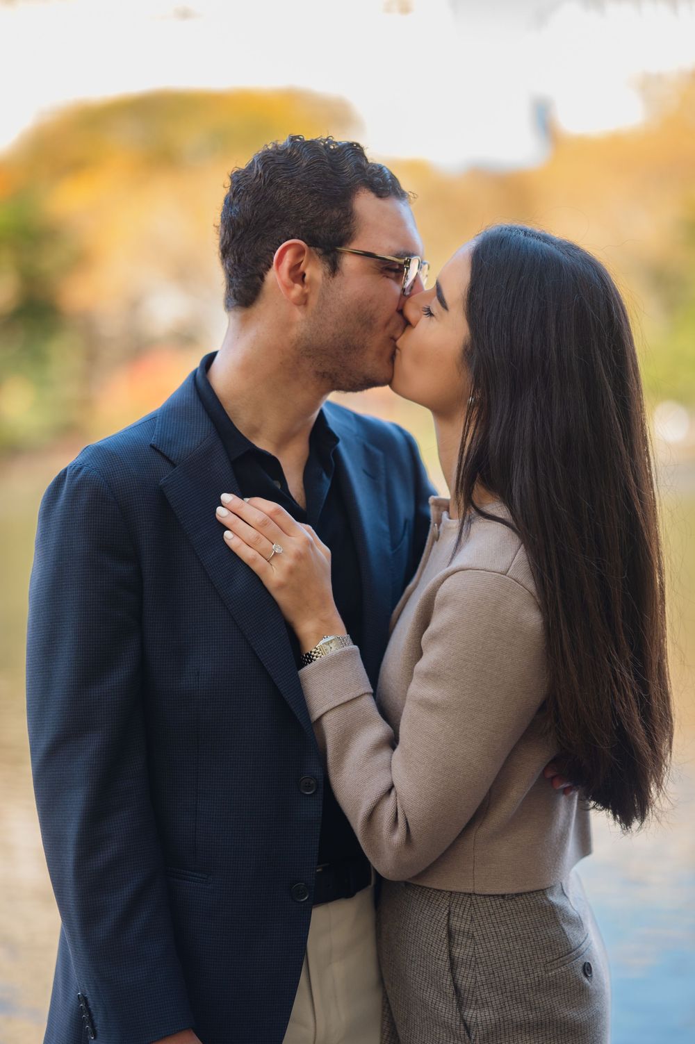 Couple sharing a romantic kiss outdoors during autumn engagement photo session in a park.