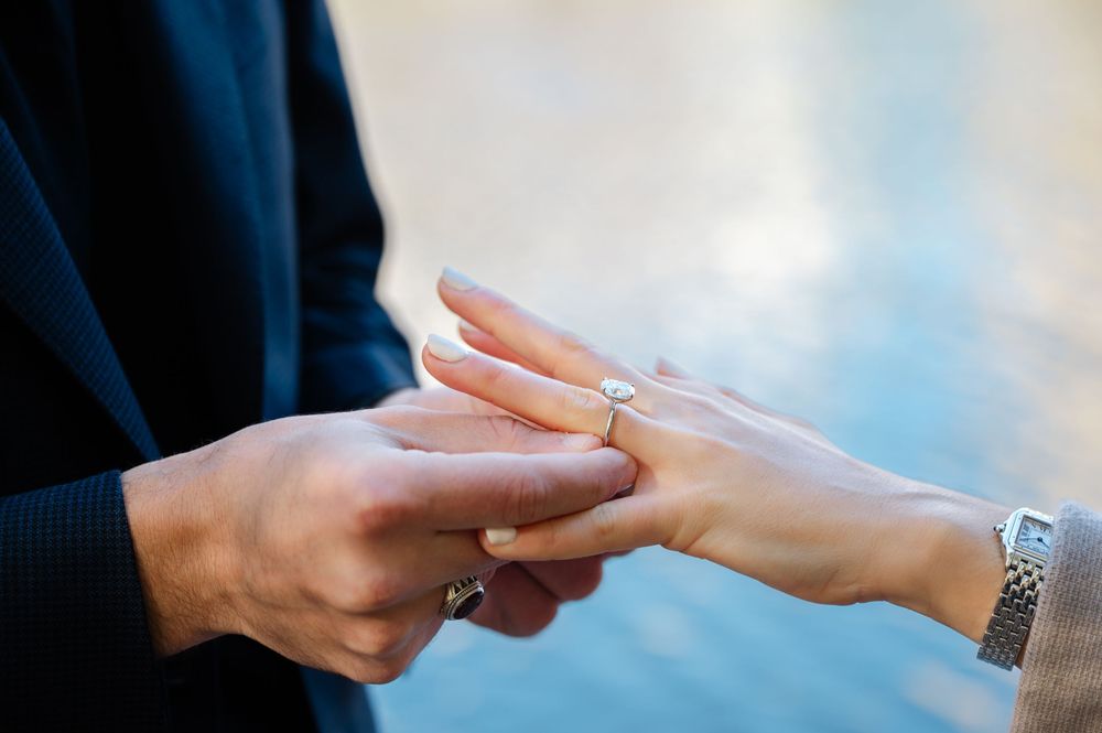 Close-up of a man placing a diamond engagement ring on a woman's finger during a marriage proposal.