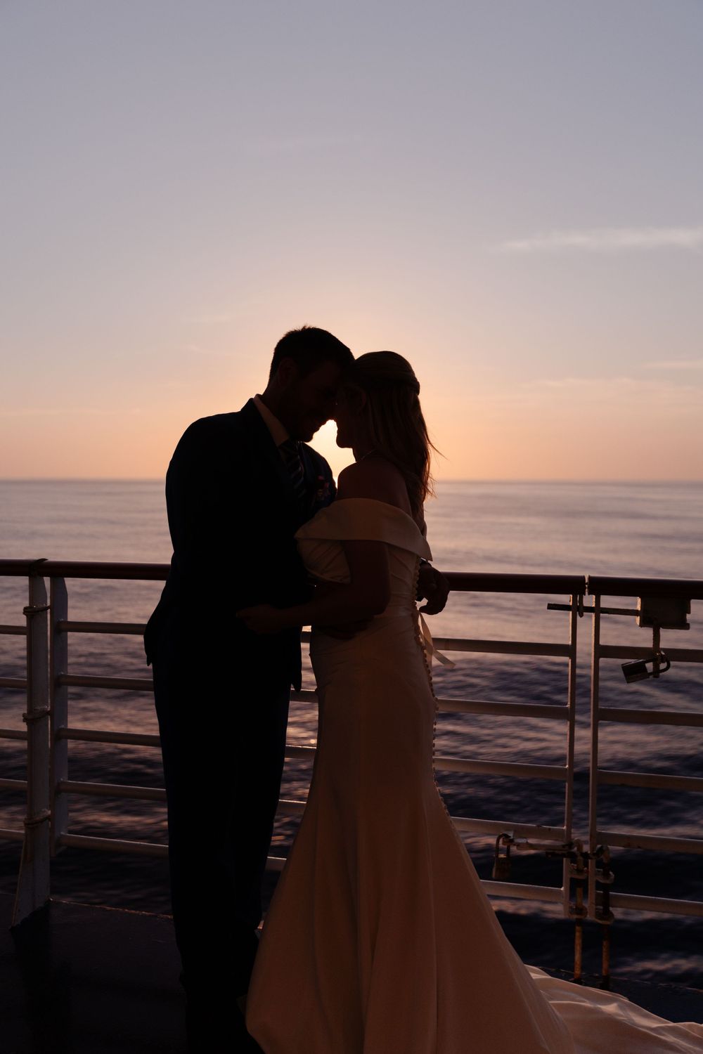A bride and groom kiss on the deck of a cruise ship at sunset.